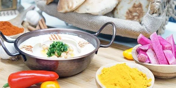 Al Ameer's hummus topped with chickpeas and parsley in a copper dish, served with pita bread, pickled turnips, and spices