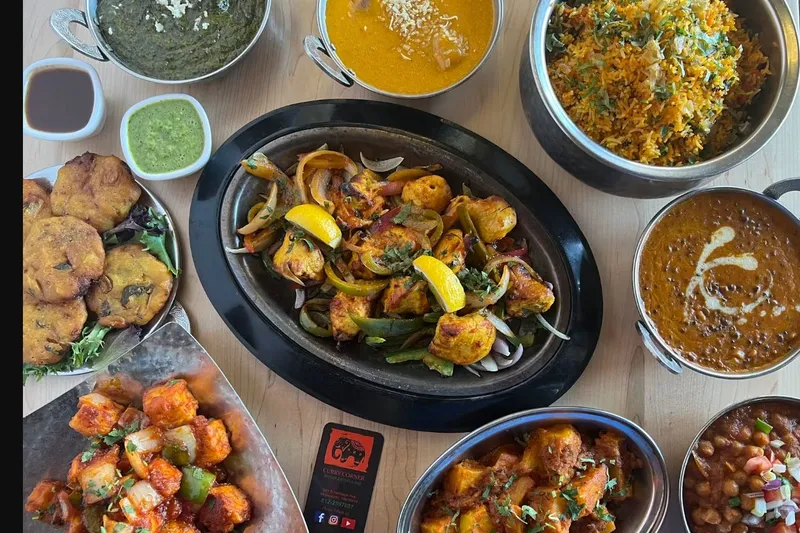 Indian curries, biryani, tandoori dishes, pakoras, and chutneys arranged on a table at Curry Corner