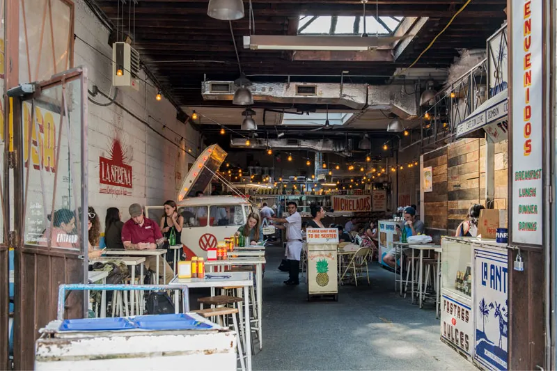 The interior of Tacombi's Nolita location, with its vintage Volkswagen van taco bar, string lights, communal tables, and hand-painted 'Bienvenidos' signage
