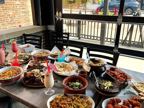 Table spread of Usmania Fine Dining dishes and lassi drinks by a window overlooking Devon Avenue