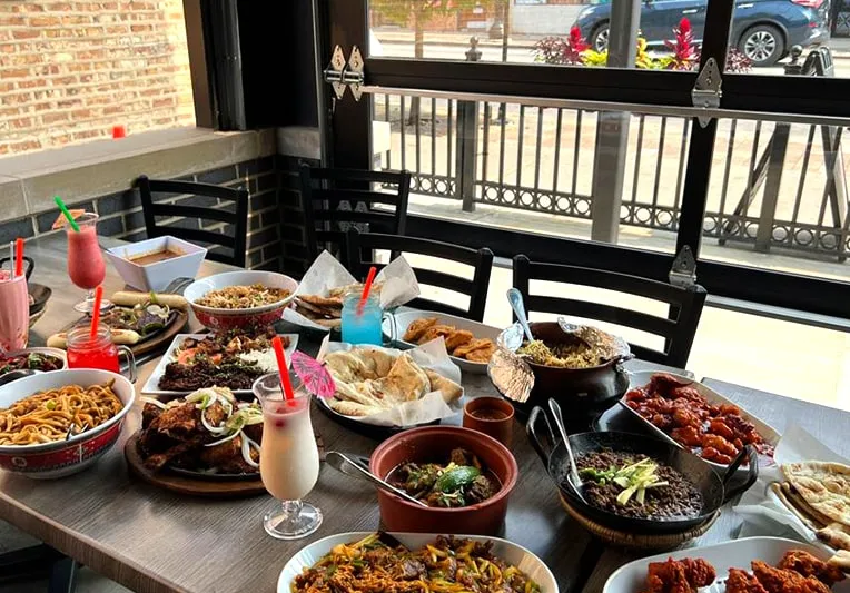 Table spread of Usmania Fine Dining dishes and lassi drinks by a window overlooking Devon Avenue