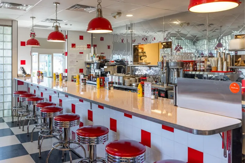 Red stools along the counter of Goober's Diner, with a checkerboard floor and red pendant lamps
