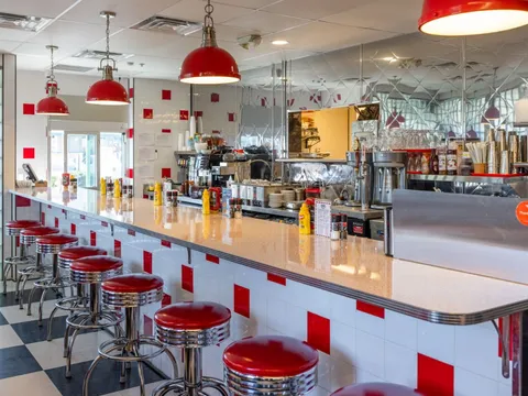 Red stools along the counter of Goober's Diner, with a checkerboard floor and red pendant lamps
