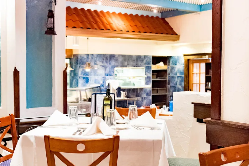 Blue-and-white Santorini-style dining room at Greek Islands in Chicago's Greektown, with white-linen tables, wooden chairs and a tiled open kitchen