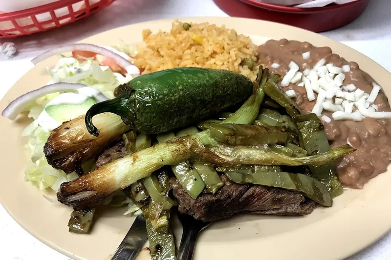 A carne asada plate at Taquería La Auténtica with grilled skirt steak, grilled green onions and a whole jalapeño, Mexican rice, and refried beans topped with shredded cheese