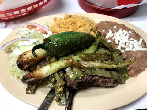 A carne asada plate at Taquería La Auténtica with grilled skirt steak, grilled green onions and a whole jalapeño, Mexican rice, and refried beans topped with shredded cheese