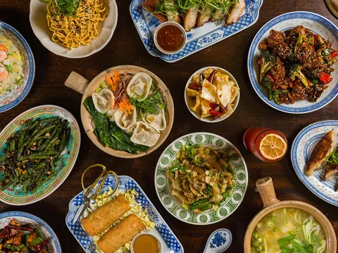 Overhead spread of dishes at Kings County Imperial including dumplings, noodles, dry-fried long beans, fried rice, spring rolls, and a claypot soup