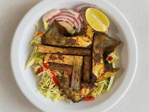 A plate of tawa fish fry — spiced pan-fried fish pieces over shredded cabbage with sliced red onion and a lime wedge — at UlavacharU Indian Restaurant in Frisco, Texas