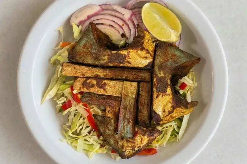 A plate of tawa fish fry — spiced pan-fried fish pieces over shredded cabbage with sliced red onion and a lime wedge — at UlavacharU Indian Restaurant in Frisco, Texas