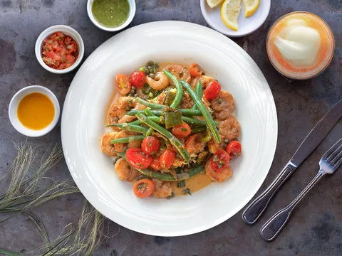 A plated shrimp dish with green beans, cherry tomatoes and salsas at Aqui Cal-Mex