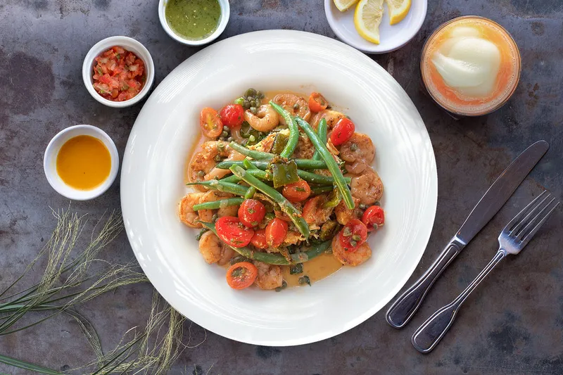 A plated shrimp dish with green beans, cherry tomatoes and salsas at Aqui Cal-Mex