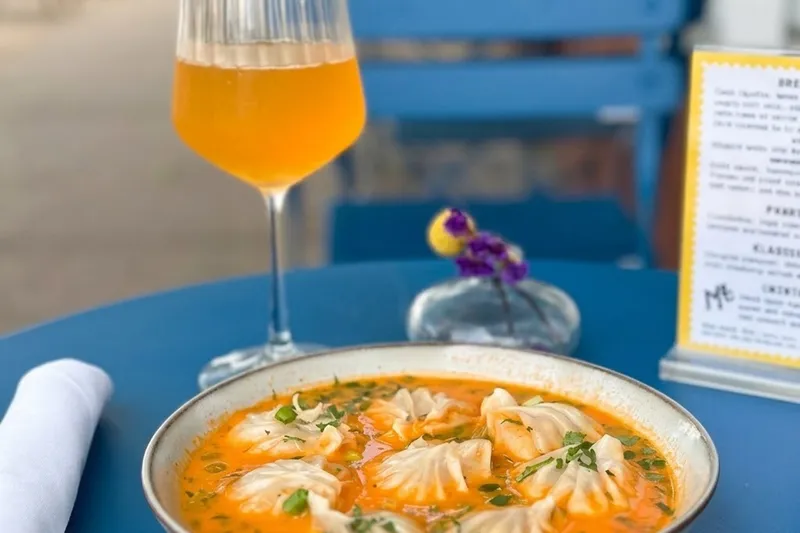 Jhol momo — steamed dumplings in a spiced tomato broth — served with a drink on an outdoor table at Makalu Boston