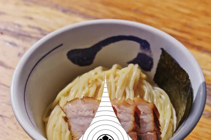 Tsukemen bowl of cold ramen noodles topped with chashu pork slices and nori, with a hand squeezing fresh lime, at Tsujita LA Artisan Noodle