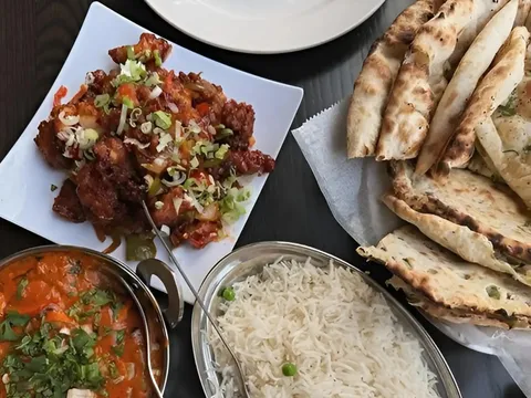 A spread of curries, rice, naan, and fried appetizers at Clay Oven.