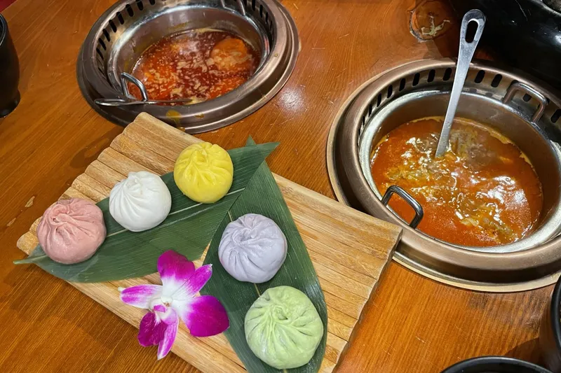 Colorful assorted soup dumplings on a wooden board beside two copper hot pot broths at Chubby Cattle
