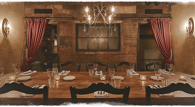 Rustic private dining room at Sotto with a long reclaimed-wood table set with glassware under a chandelier and red drapes