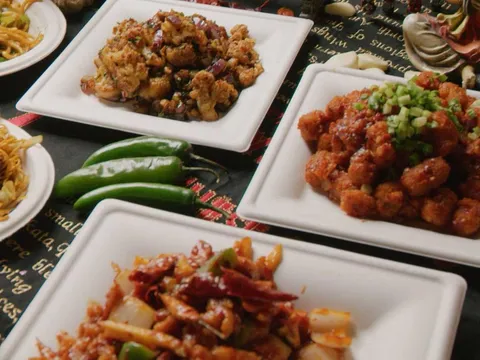 Overhead spread of Indo-Chinese dishes at Chinese Dhaba in Decatur, including gobi (cauliflower) Manchurian, chili chicken, chili paneer and Hakka noodles on white plates