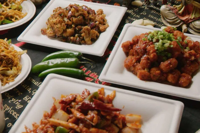 Overhead spread of Indo-Chinese dishes at Chinese Dhaba in Decatur, including gobi (cauliflower) Manchurian, chili chicken, chili paneer and Hakka noodles on white plates