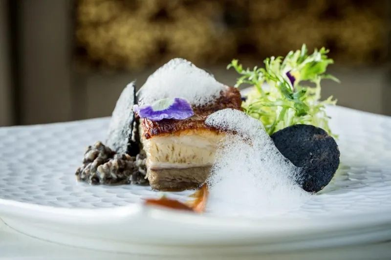Plated crispy pork belly starter with black-lentil, herb foam and greens at All Spice, San Mateo