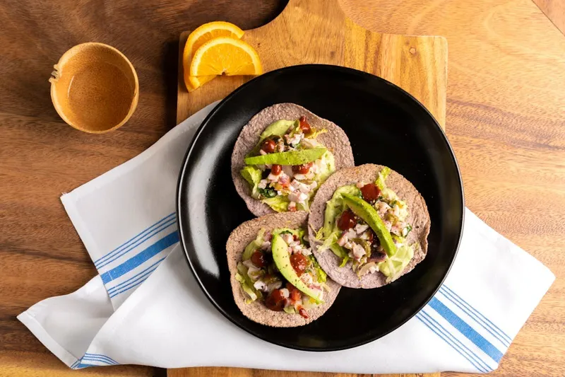 Three tacos arranged on a black plate at Bakan Wynwood