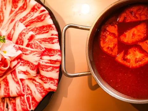 Top-down view of a marbled beef platter beside a tomato-broth hot pot at Little Sheep Hot Pot & Bar