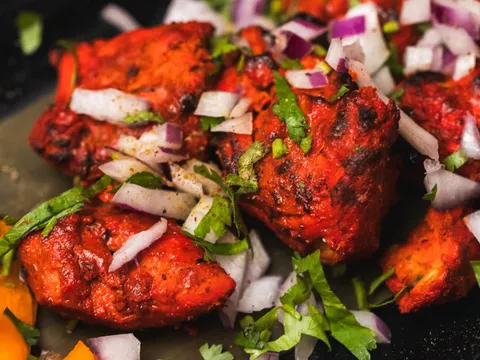 Close-up of tandoori chicken tikka topped with chopped red onion and cilantro at Tikka Indian Grill