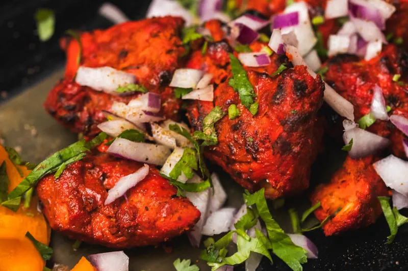 Close-up of tandoori chicken tikka topped with chopped red onion and cilantro at Tikka Indian Grill