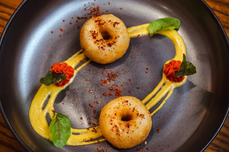 Golden fried medu vada fritters over a saffron-yellow sauce with micro herbs at Indian Accent
