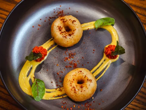 Golden fried medu vada fritters over a saffron-yellow sauce with micro herbs at Indian Accent