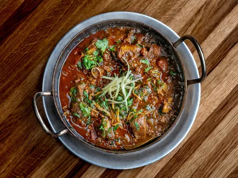 Curry served in a steel karahi on a wooden table at Dhamaka