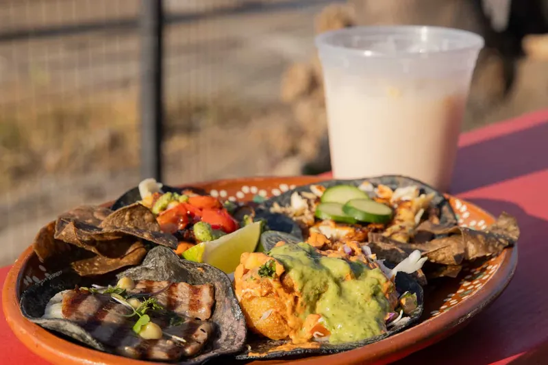 A clay plate of Villa's Tacos blue-corn tacos with grilled fillings, salsas, tortilla chips, lime and cucumber, next to a cup of agua fresca
