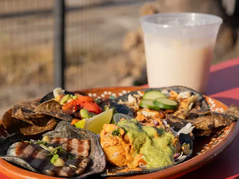 A clay plate of Villa's Tacos blue-corn tacos with grilled fillings, salsas, tortilla chips, lime and cucumber, next to a cup of agua fresca