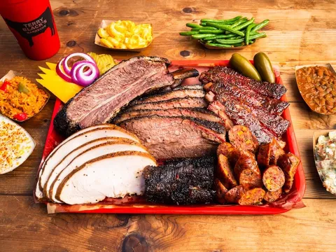 A tray of Terry Black's Barbecue in Austin loaded with sliced brisket, pork ribs, sausage and turkey, surrounded by sides