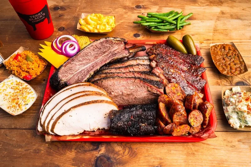 A tray of Terry Black's Barbecue in Austin loaded with sliced brisket, pork ribs, sausage and turkey, surrounded by sides