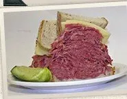 A towering corned beef sandwich with a pickle at Slyman's