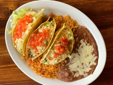 Plate of three crispy tacos topped with lettuce and diced tomato, served with Spanish rice and refried beans at Casa Corona in Fresno