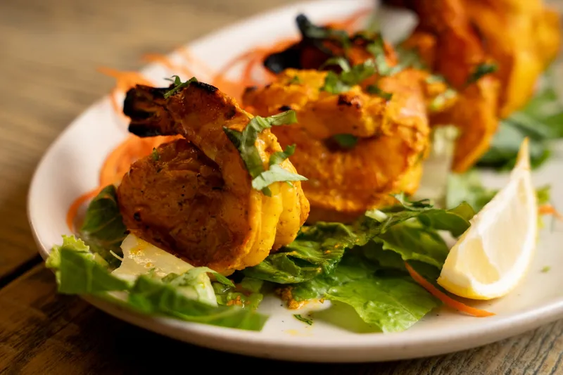 Char-grilled tandoori chicken tikka skewers on a bed of lettuce with lemon at Bollywood Bistro
