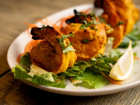 Char-grilled tandoori chicken tikka skewers on a bed of lettuce with lemon at Bollywood Bistro