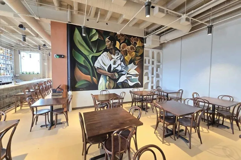 Dining room at Santoro in Omaha, with wooden bentwood chairs and tables and a large mural of a woman holding calla lilies on the wall