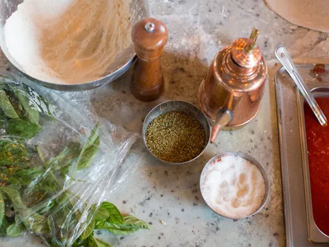 Il Lazzarone pizza-making ingredients on a marble counter — flour, oregano, sea salt, San Marzano tomato sauce, fresh basil and a copper olive-oil pourer