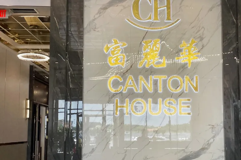 Marble reception wall with illuminated gold Canton House (富麗華) signage and gilded guardian lion statues inside the Chamblee restaurant