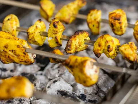 Skewers of marigold-yellow tandoori chicken tikka cooking over glowing charcoal at Star of India in Salt Lake City