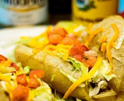 Close-up of Teka Molino puffy tacos filled with meat and topped with shredded lettuce, diced tomato and cheddar cheese, with bottles of Modelo beer behind