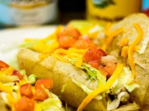 Close-up of Teka Molino puffy tacos filled with meat and topped with shredded lettuce, diced tomato and cheddar cheese, with bottles of Modelo beer behind
