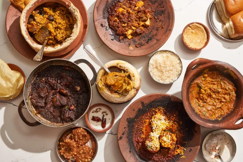 A spread of dishes at Masalawala & Sons in Brooklyn — biryani, dark braised meat, curries and dal in clay and steel vessels with rice, pao and papad