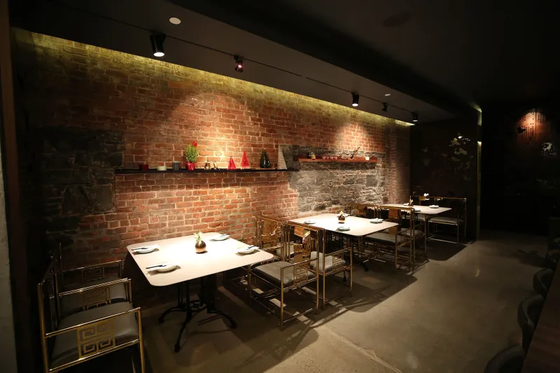 Interior dining room at uluh in the East Village with exposed brick and stone walls, gold-framed fretwork chairs and marble-topped tables set for service