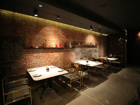 Interior dining room at uluh in the East Village with exposed brick and stone walls, gold-framed fretwork chairs and marble-topped tables set for service