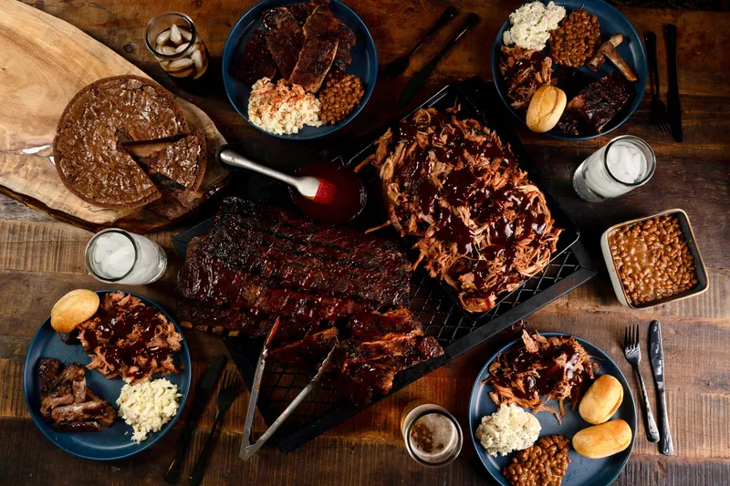 Overhead spread of Corky's Ribs & BBQ Memphis showing a rack of glazed pork ribs, pulled pork with sauce, coleslaw, baked beans, rolls, sliced brisket and a chocolate pie on a wooden table