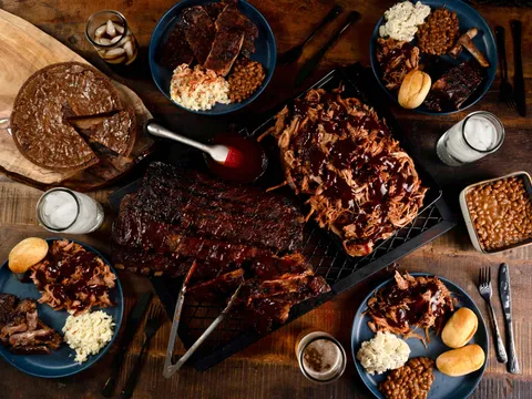 Overhead spread of Corky's Ribs & BBQ Memphis showing a rack of glazed pork ribs, pulled pork with sauce, coleslaw, baked beans, rolls, sliced brisket and a chocolate pie on a wooden table