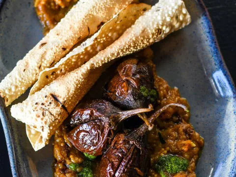 Baby Brinjals — roasted stuffed baby eggplants over spiced masala with green chutney and rolled papadum on a blue ceramic plate at Cheeni in downtown Durham